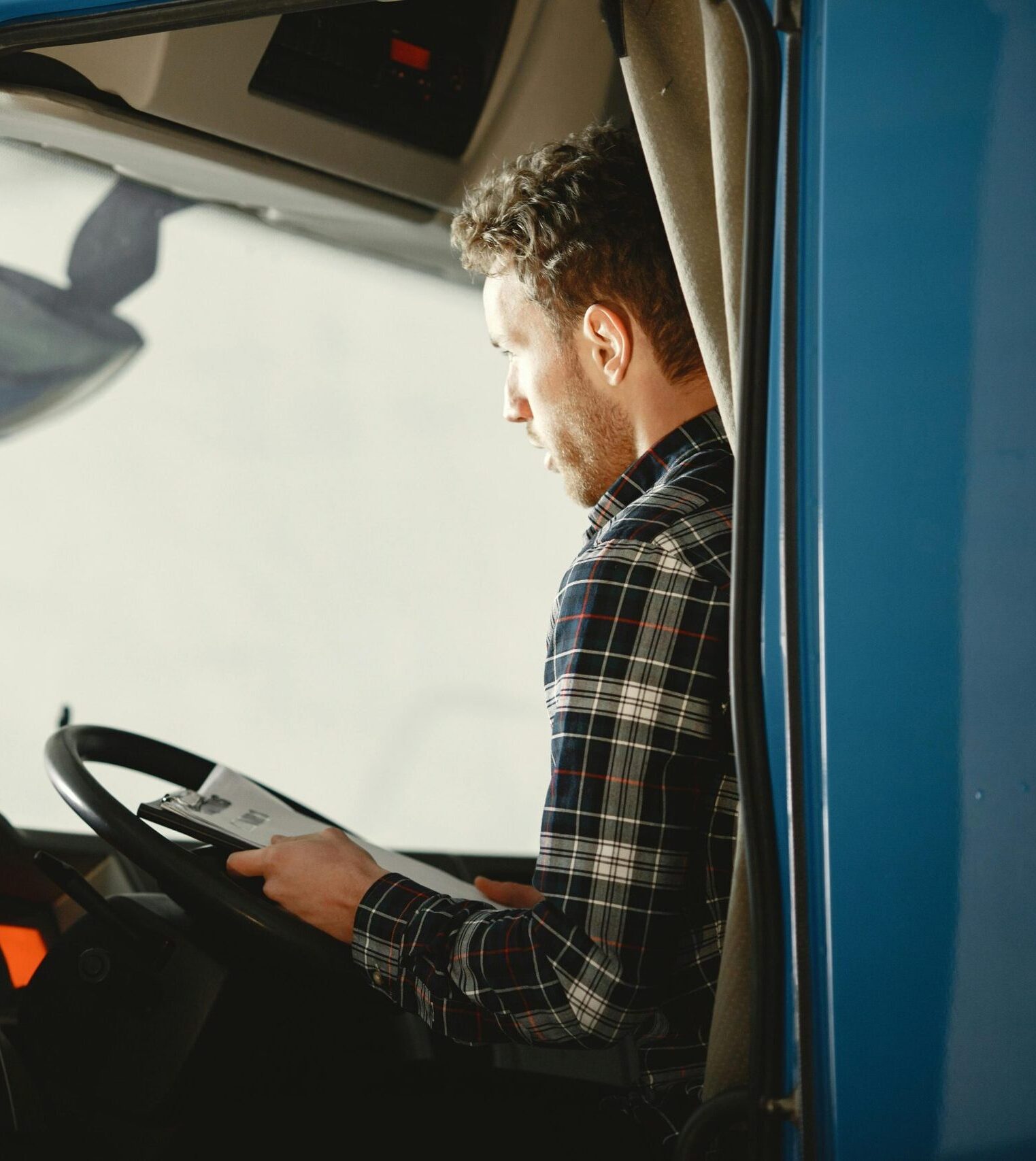 A man sitting in a truck cabin reading a document inside a blue truck, showcasing focused driving preparation.